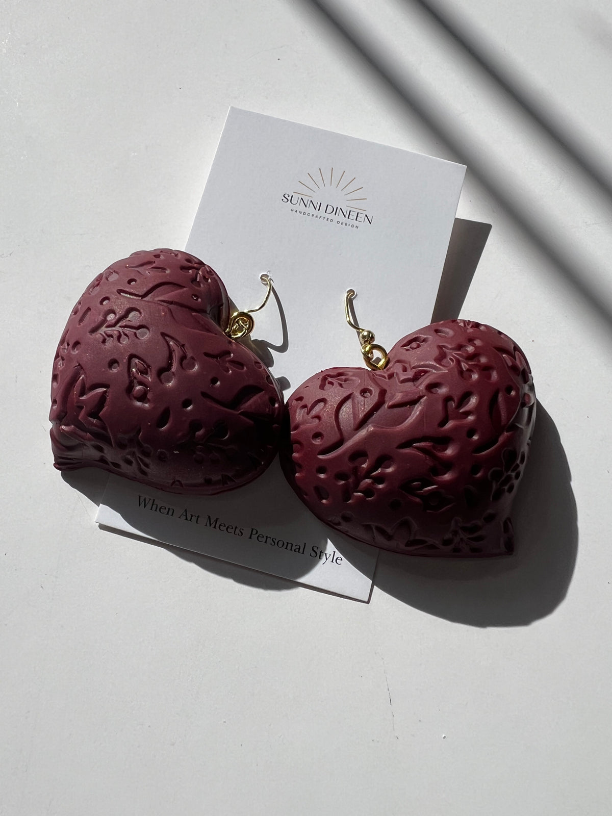 The Puffy Heart Statement Earrings in wine, displayed on a white earring card on a white surface, handmade by Sunni Dineen.