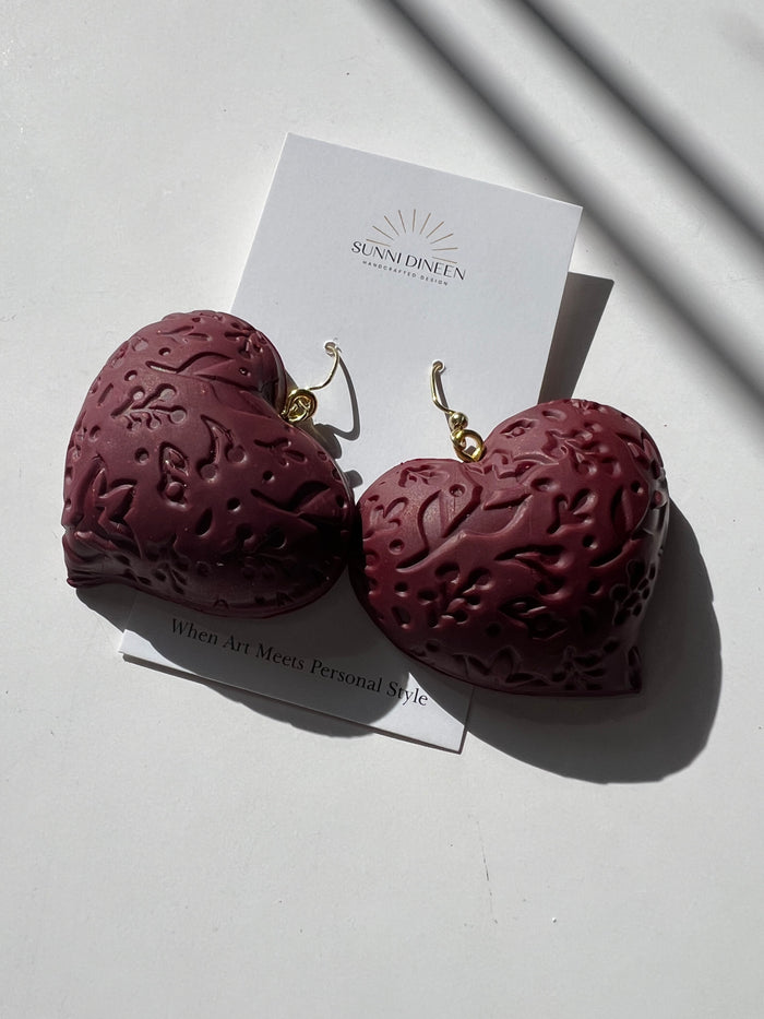The Puffy Heart Statement Earrings in wine, displayed on a white earring card on a white surface, handmade by Sunni Dineen.