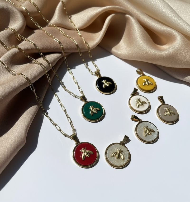 Gold queen honeybee pendants in and necklaces shown in various color choices displayed over white surface and beige silk fabric by SGB x SDHD.