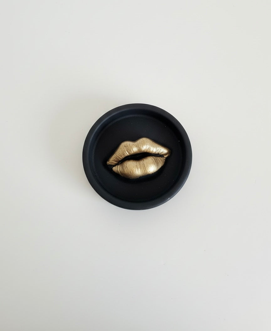 A black Sculptural Lips Incense Holder with gold lips, handmade by Sunni Dineen, displayed on a white surface.
