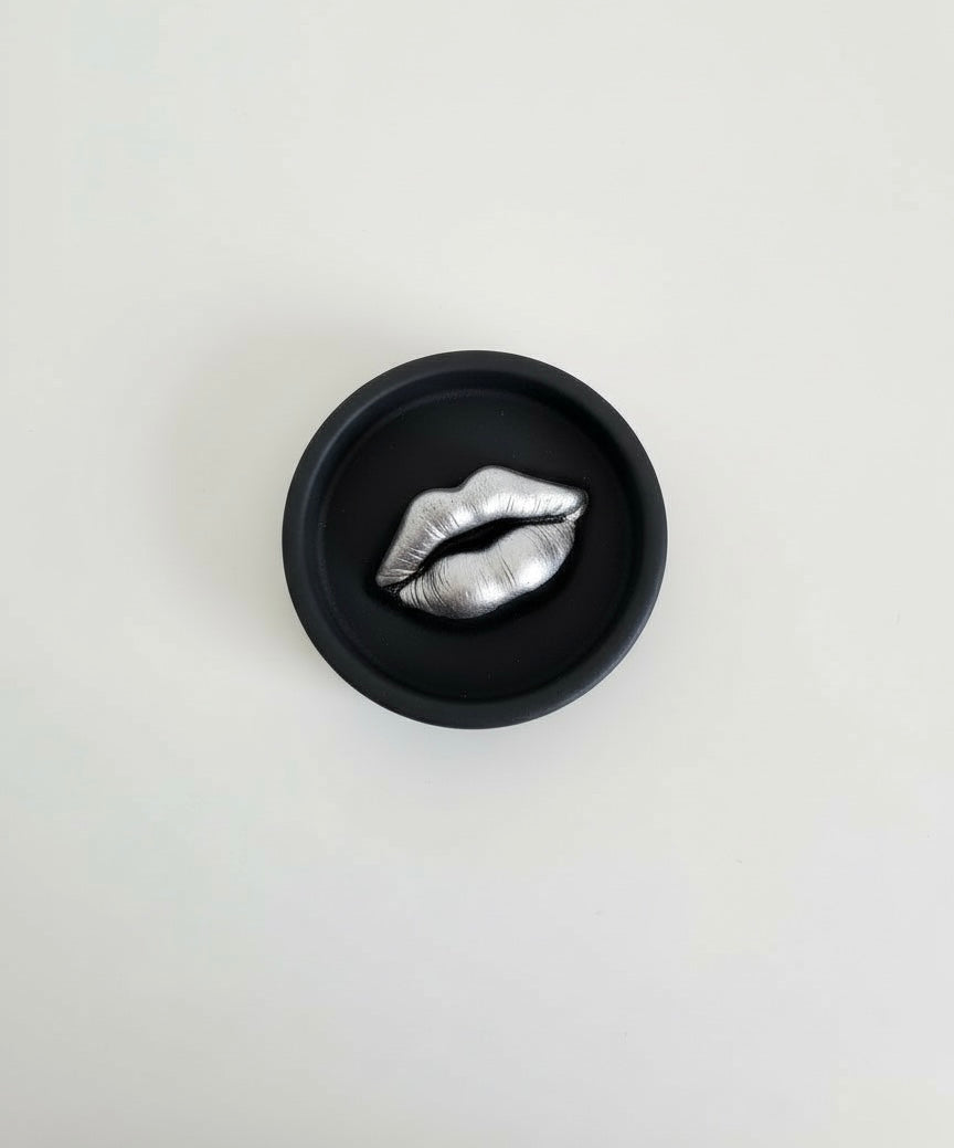A black Sculptural Lips Incense Holder with silver lips, handmade by Sunni Dineen, displayed on a white surface.