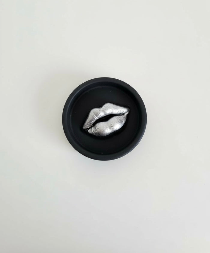 A black Sculptural Lips Incense Holder with silver lips, handmade by Sunni Dineen, displayed on a white surface.