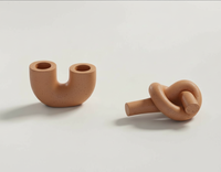 A terracotta U-shaped candlestick holder & terracotta knot candlestick holder handmade by Sunni Dineen, displayed on a white surface.