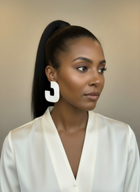 A model styled wearing a white blouse and a pair of white 'Gia' statement earrings, handmade by Sunni Dineen, against a beige background.