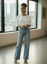 A woman with braided up-do standing next to a window in a room styled wearing a white t-shirt and wide-legged denim jeans and a pair of blue & white patterned 'Kalani' statement earrings, handmade by Sunni Dineen.